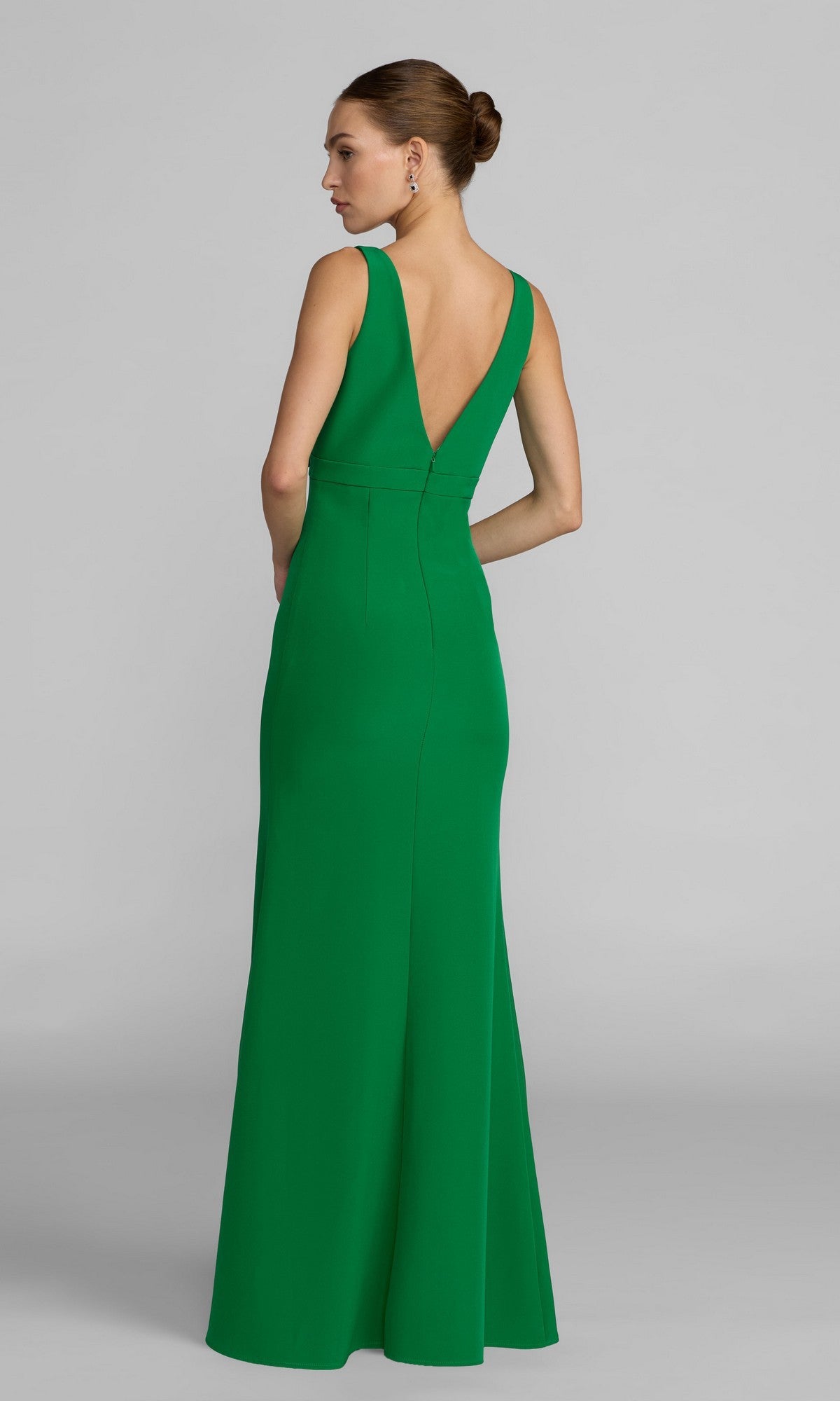 A woman wears the Mac Duggal 2371 long formal dress, featuring sleeveless green crepe fabric and a floor-length silhouette with a deep V-back design.